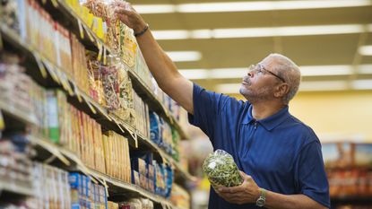 An older man reaches for something on a higher shelf at the grocery store.