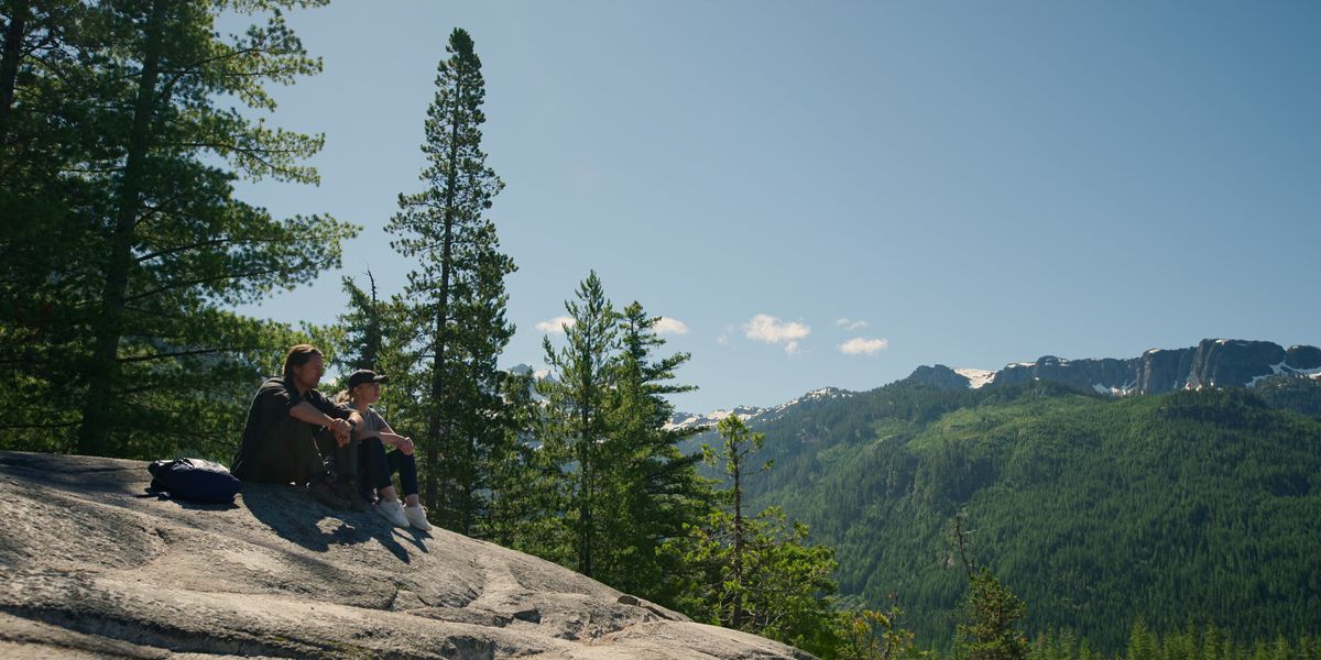 Brie and Brady sit on a rock with a picturesque forest background behind them.