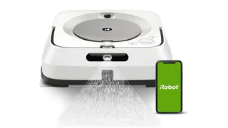 The iRobot Braava Jet M6 robot mop vacuum spraying water beside a mobile device displaying the iRobot app