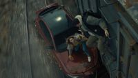 A man and a woman attempting to board a train from their stricken car that is being dragged along the track.