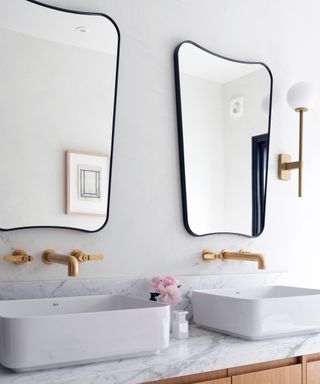 two black rimmed wall mirrors hung over double white basins in bathroom