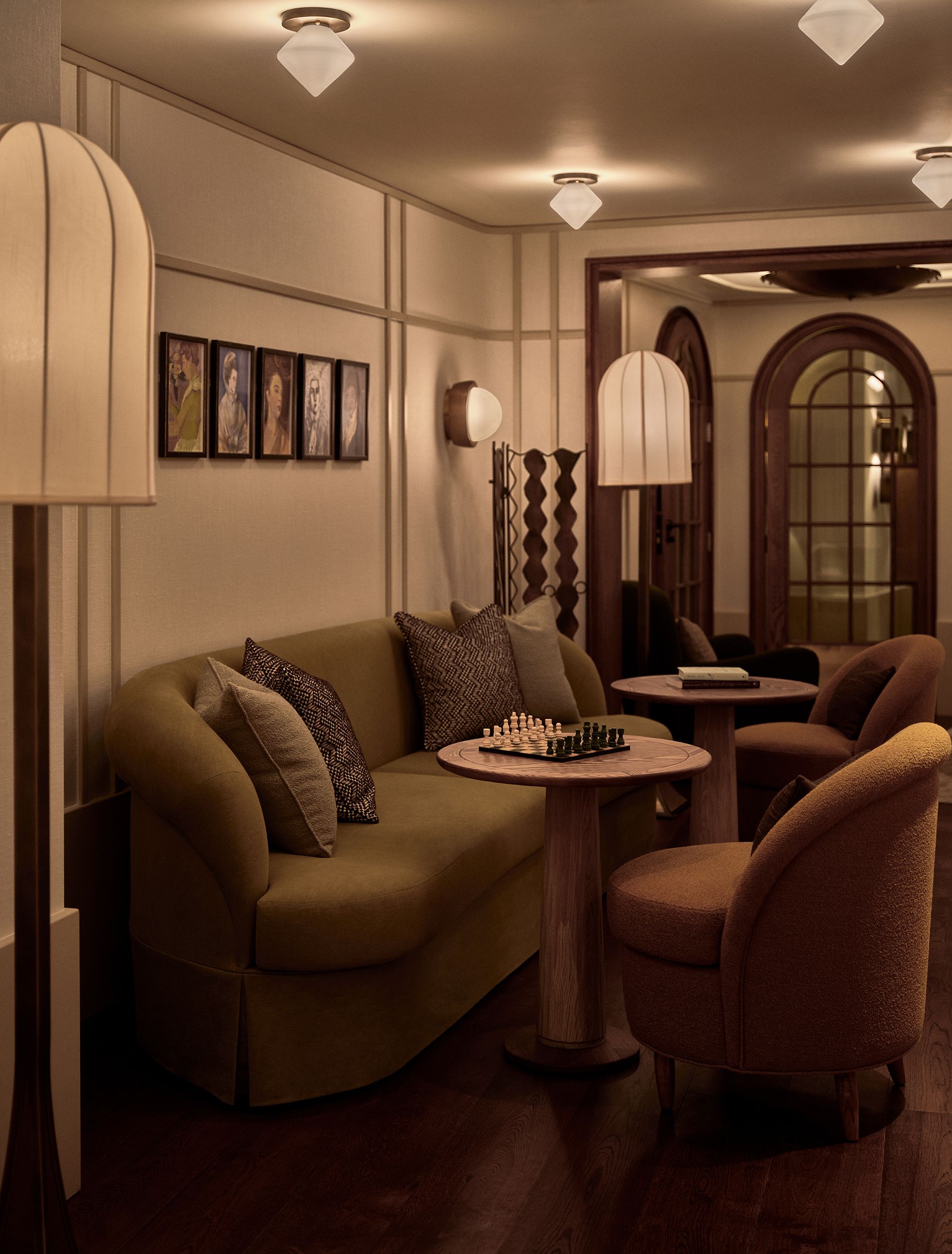 A warmly decorated, vaguely Art Deco-reminiscent hotel features plush textiles in green tones, beige walls, and sculptural lighting.