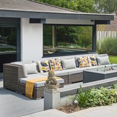 a decked area of a garden with a large corner outdoor sofa with cushions and a firepit table