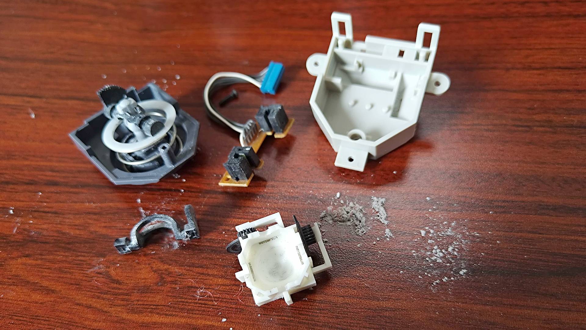 N64 joystick dismantled into parts on woodgrain desk with worn plastic dust residue.