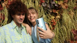 A Moto G62 being used to frame a group selfie of a man and a woman