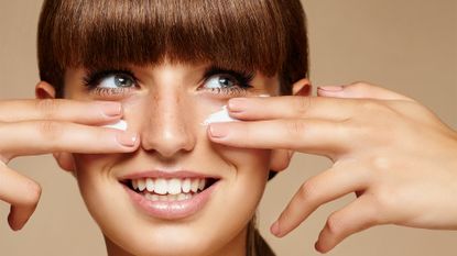 studio shot of a young brunette applying cream on her face during skincare step - stock photo