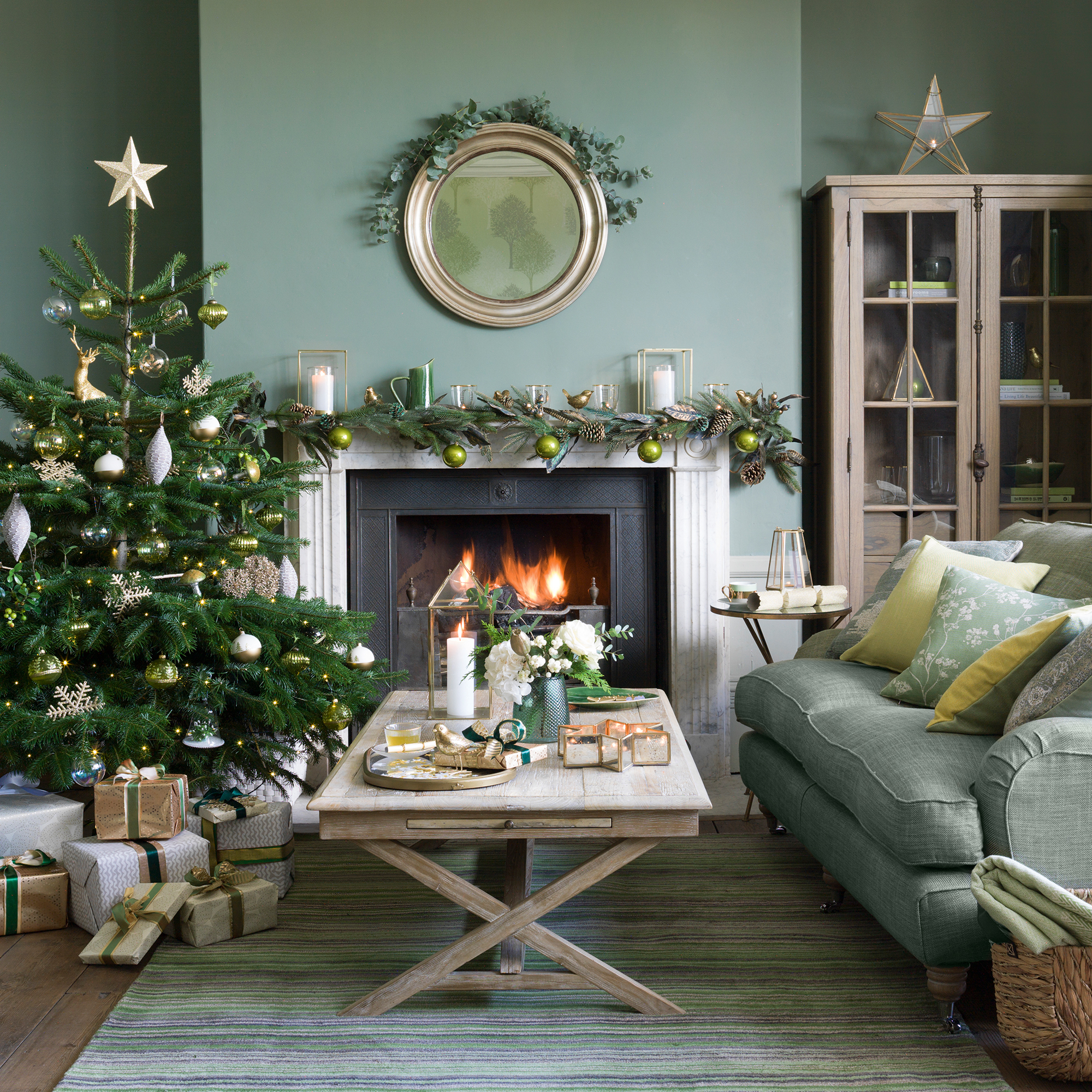 Green living room with wooden coffee table and green sofa with a real christmas tree next to an open fire