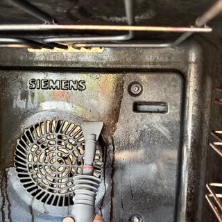 steam cleaner cleaning an oven interior with a scraper attachment