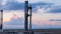 A towering SpaceX Starship rocket stands at Starbase's Pad 2, bathed in chrome against a dusk/dawn blue sky.