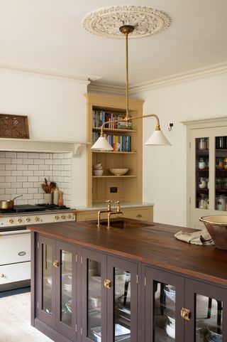 A kitchen with a wooden island, yellow shelving, and a vintage-style light fixture in a ceiling rose