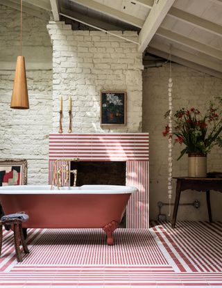 A bathroom with a freestanding bath, white painted brick walls, and a white and red tiled floor with matching tiled fireplace