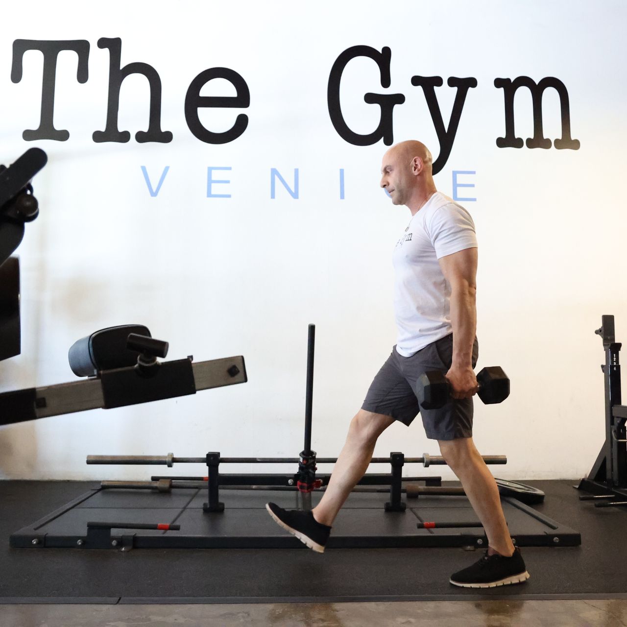 Man in gym demonstrating walking lunge exercise, holding a dumbbell