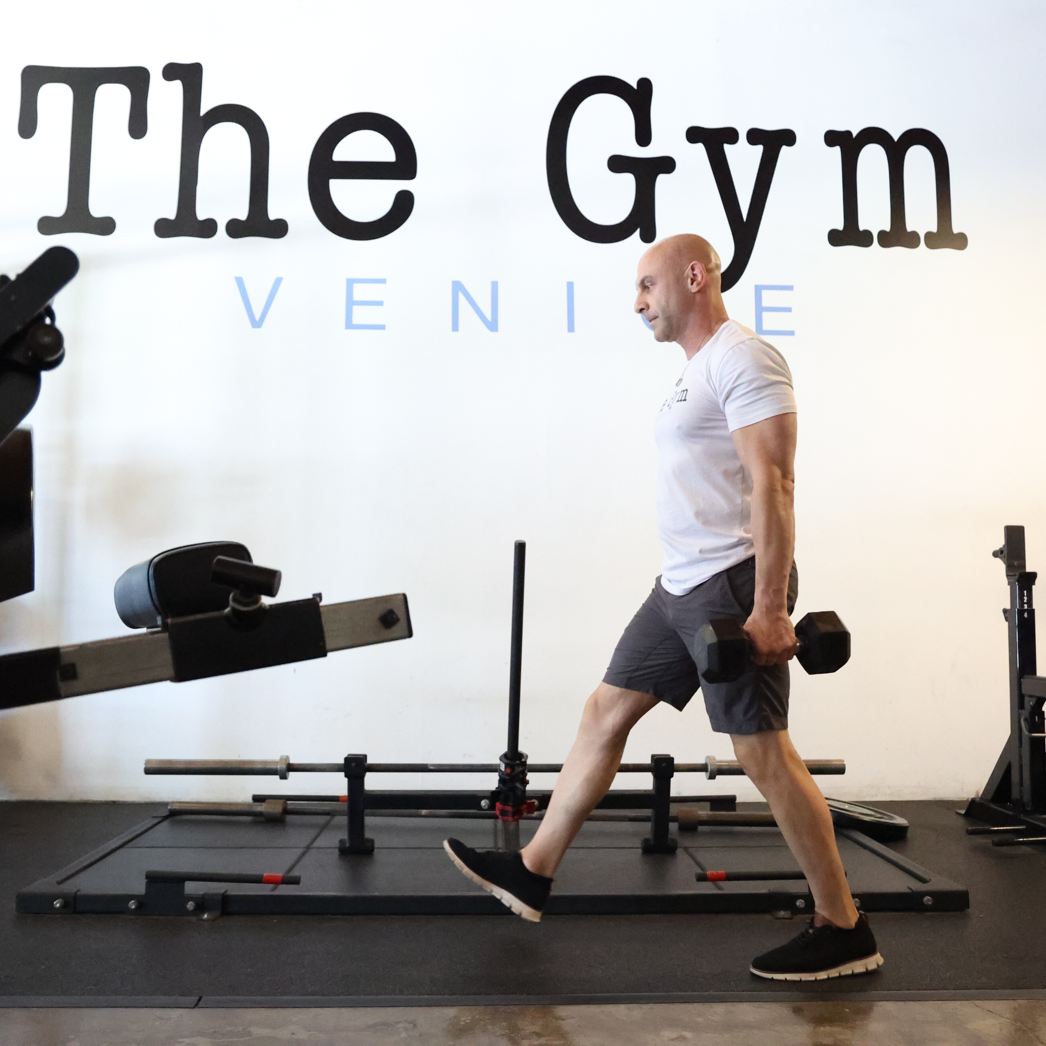 Man in gym demonstrating walking lunge exercise, holding a dumbbell