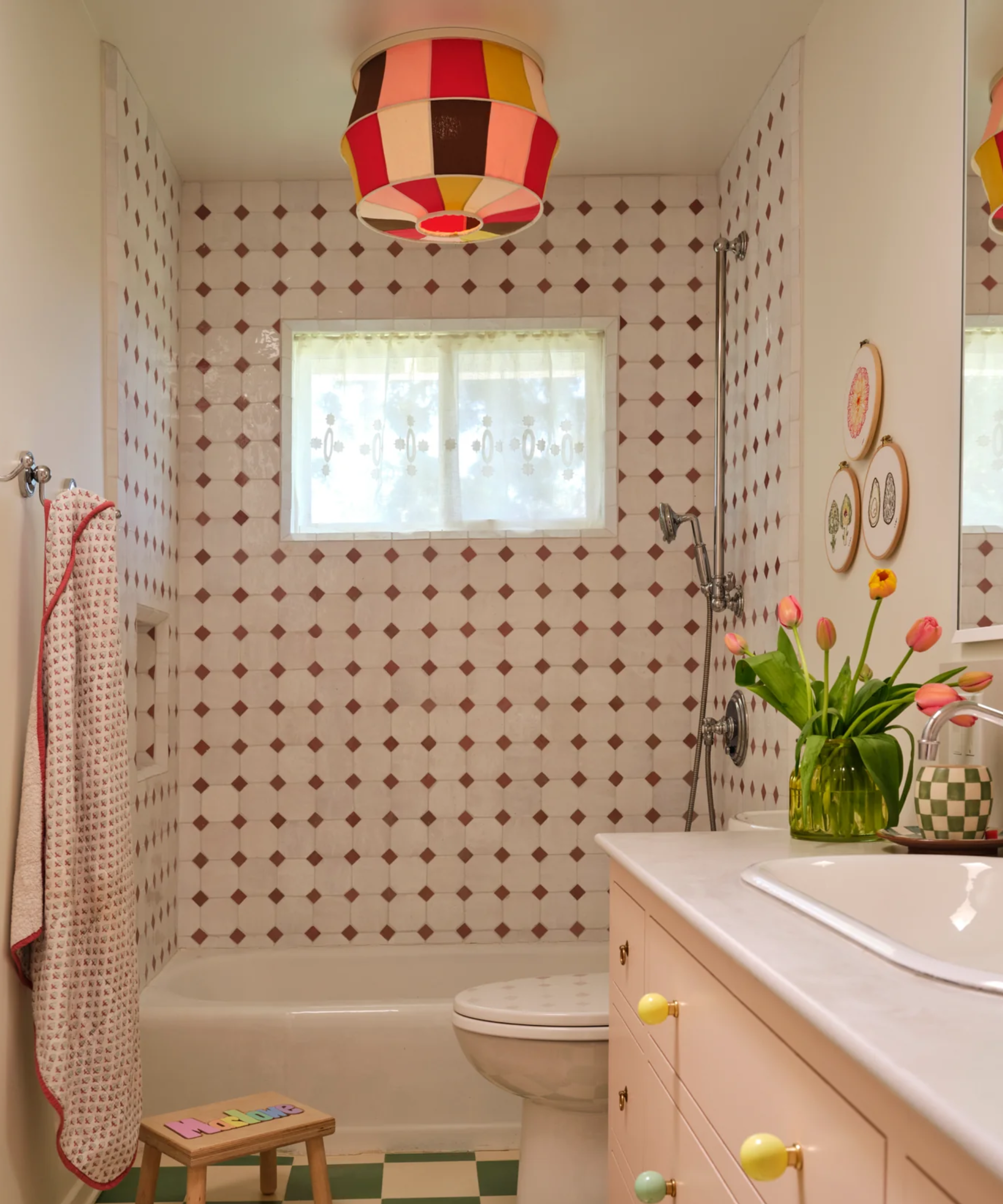 a pink bathroom with a tiled shower, a multi-colored ceiling lamp, and a vase of flowers on the sink countertop