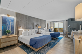 Two beds covered in white sheets and blue blankets in a large room with views of the water at Newport Harbor Island Resort in Rhode Island