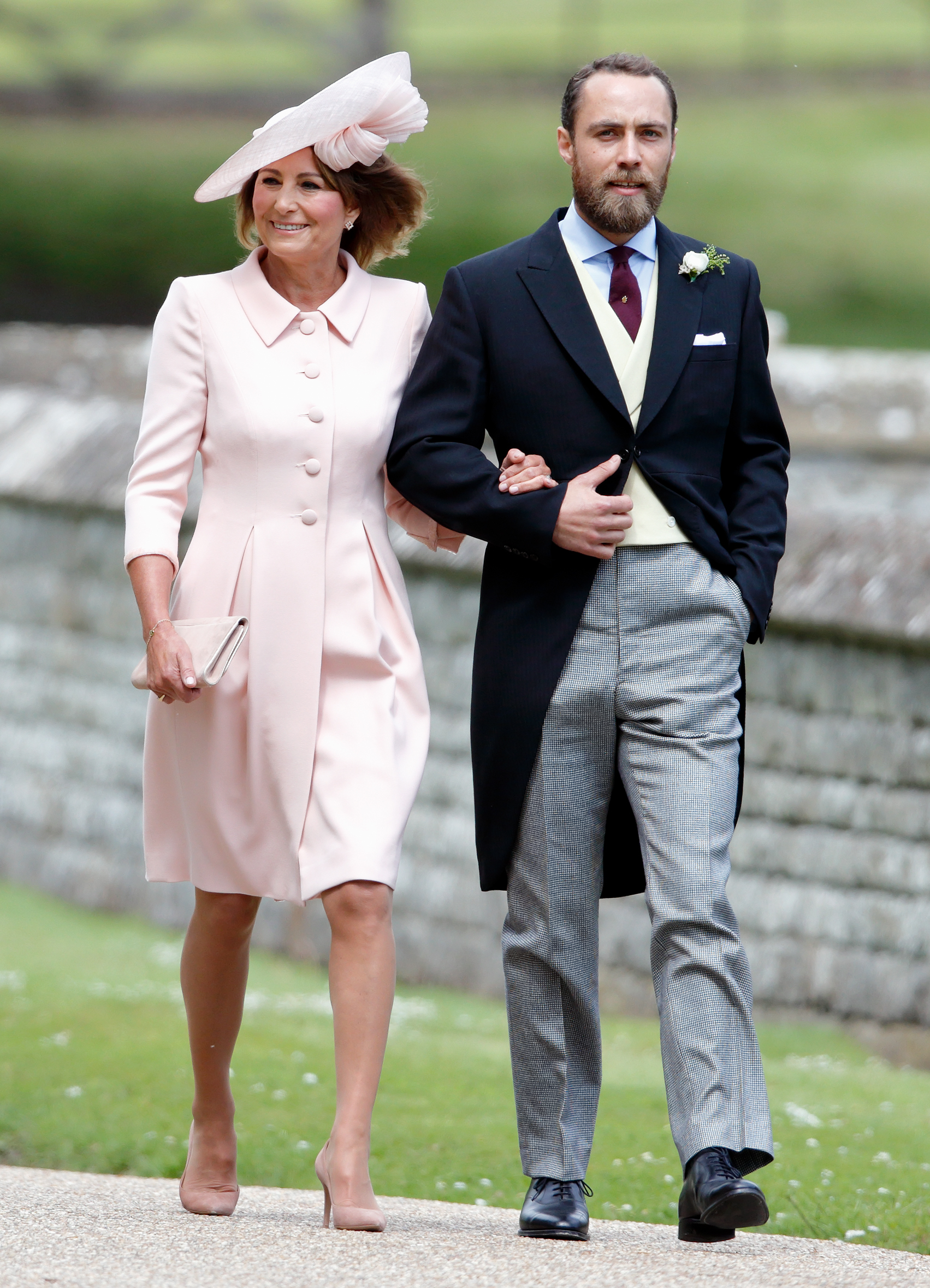 Carole Middleton wears a pink coat dress and matching hat and walks arm in arm with son James Middleton to attend Pippa Middleton's wedding