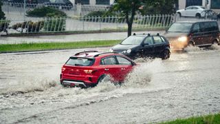 red hatchback driving through flooded road