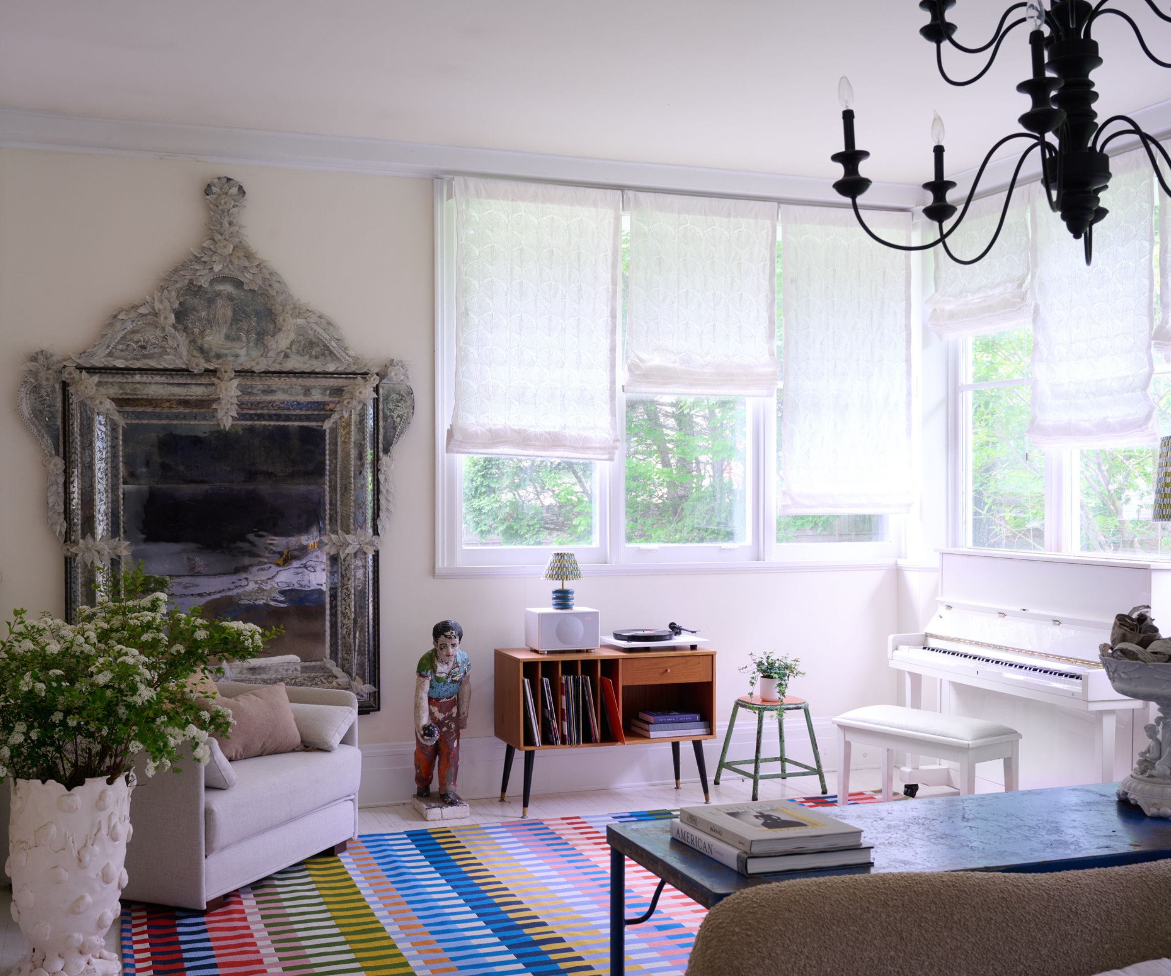 white living room with large antique mirror and striped colorful rug and mix of mid-century and traditional furniture