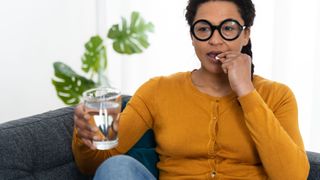 Woman taking a pill while holding a glass of water.