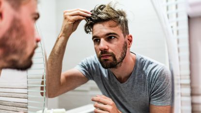 Man checks his hairline as he looks in the mirror