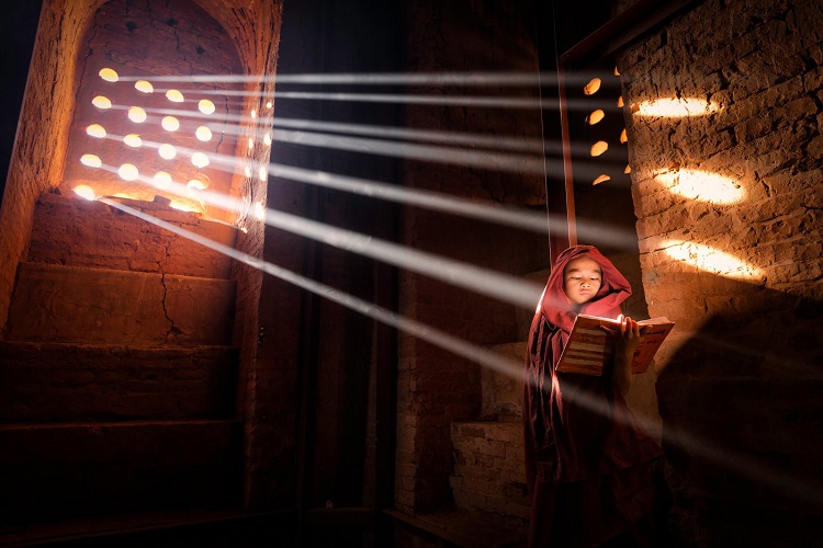 In Burma, a young monk reads from his book by the light of the window.