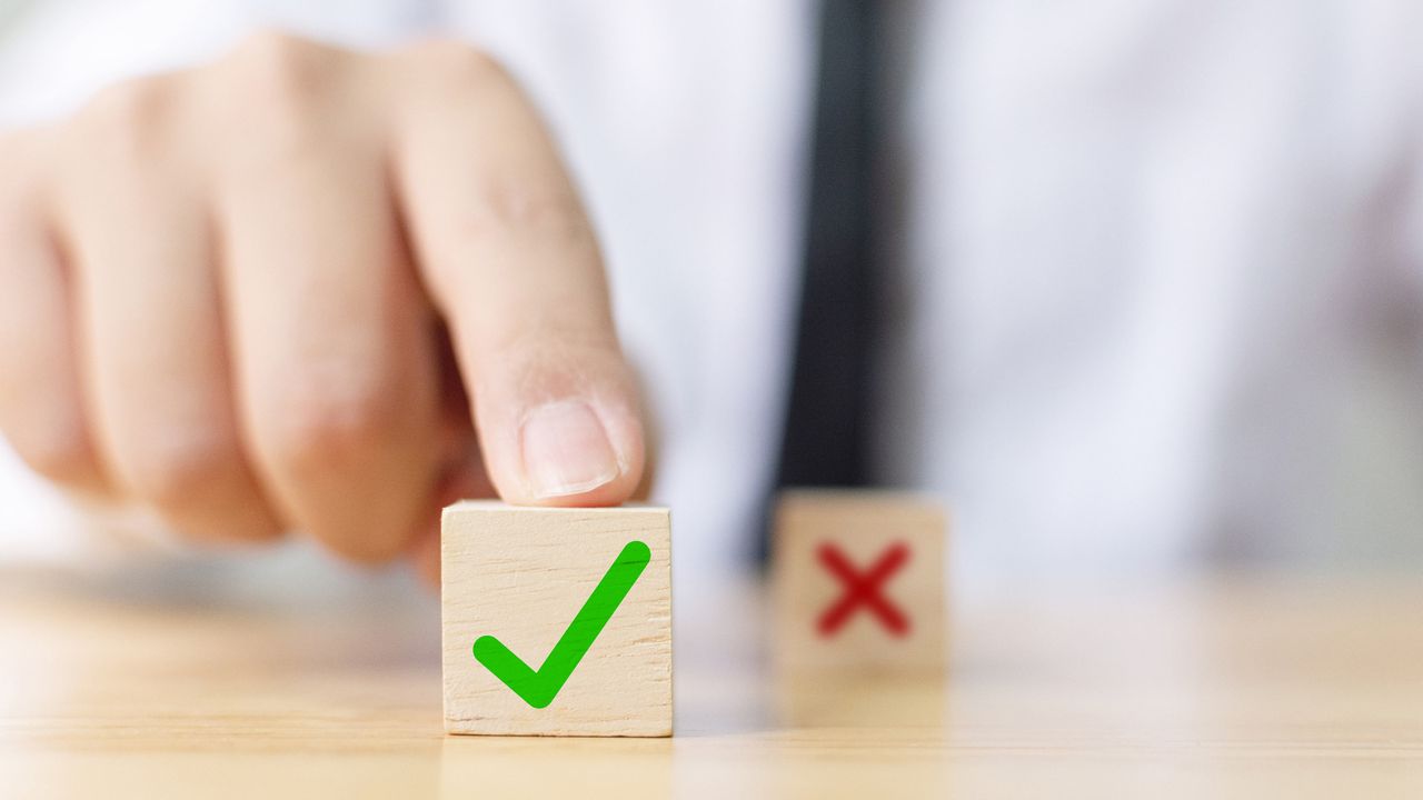 A man pushes a wooden block with a green check mark on it forward. A block with a red X is seen in the background.