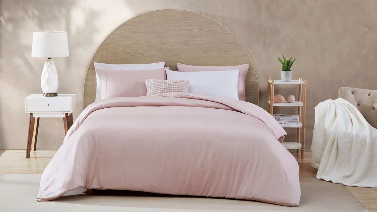 Pink and white bed sheets on a bed against a beige background. 