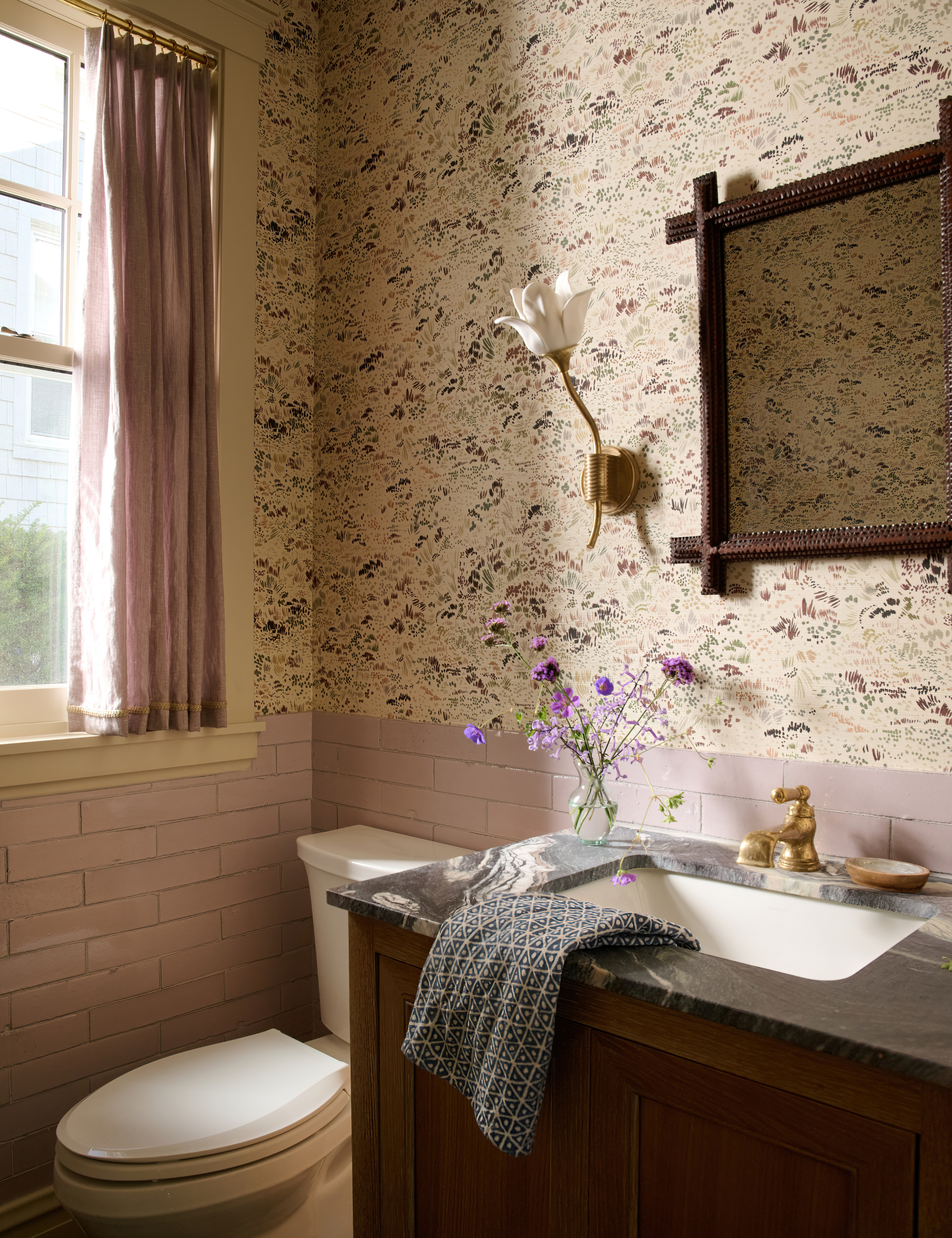 Calming guest bathroom featuring lavender subway tiles, patterned wallpaper, and fresh flowers