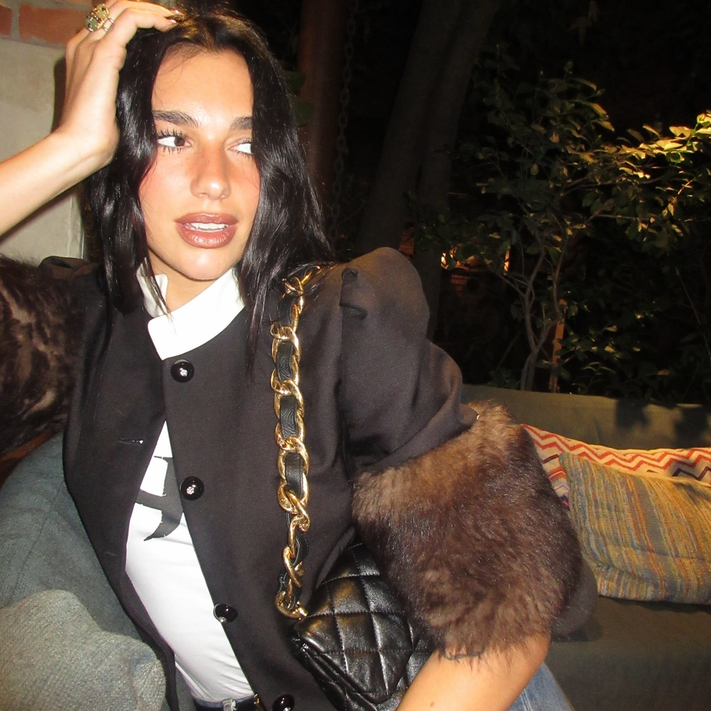 Dua Lipa wearing a jacker with furry-trimmed cuffs and a quilted black leather bag with a gold chain