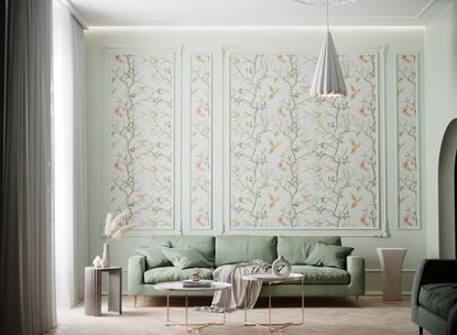 A living room with a sage green sofa and bird patterned wallpaper on the walls