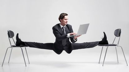 A very flexible man does the splits as he works on his laptop.