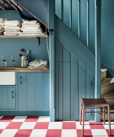 blue laundry room with checked red and white floor tiles, stool, cabinetry with sink, laundry maid, folded linen on shelf