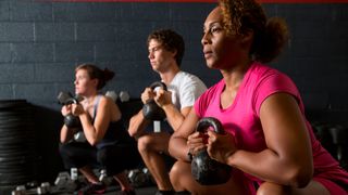 Three people in a line perform a squat holding a kettlebells by their chests