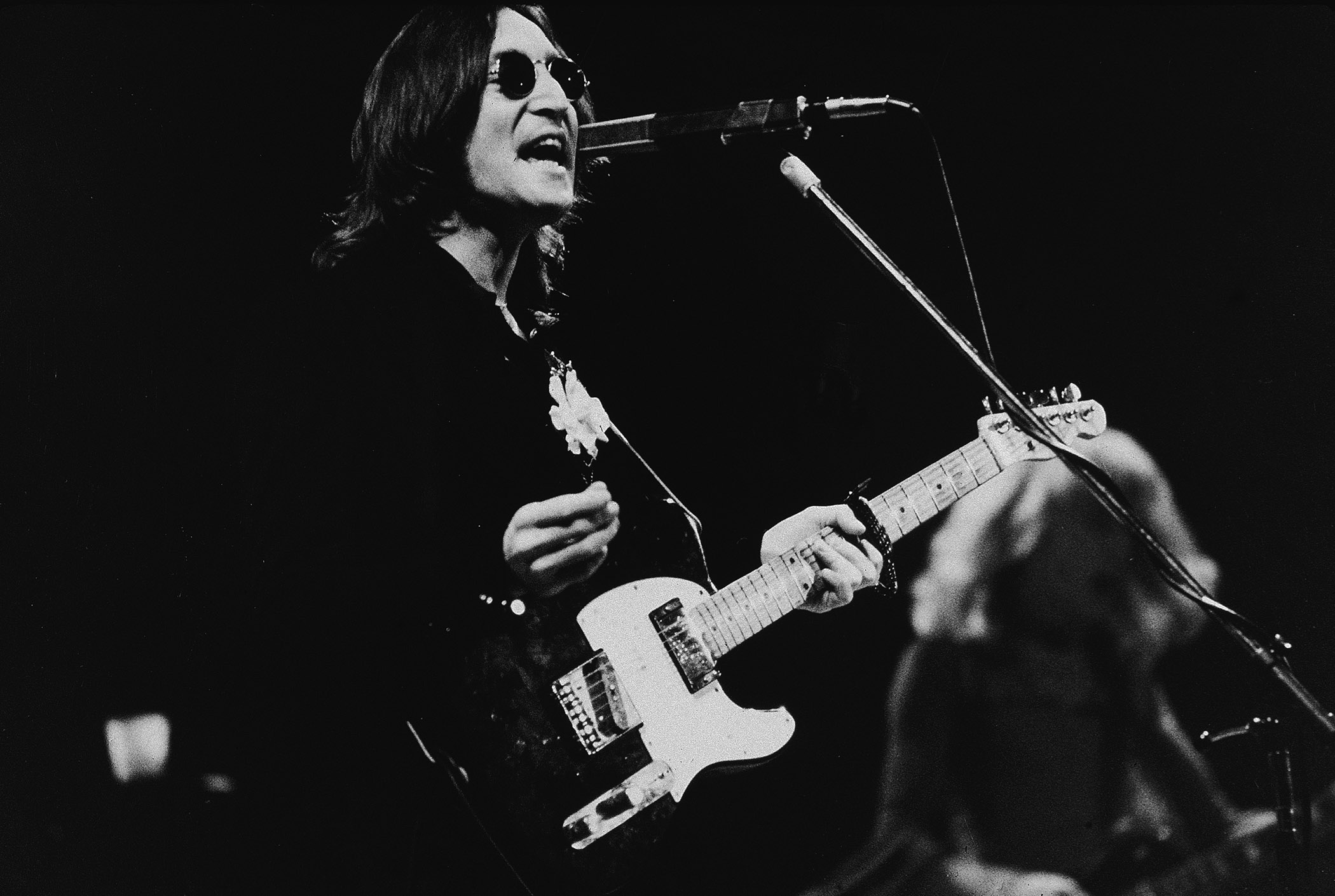 A black-and-white shot of John Lennon playing a Fender Telecaster Deluxe, live onstage during Elton John&#039;s 1974 Thanksgiving concert at Madison Square Garden