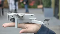 The tiny DJI Mavic Mini drone balanced on someone's upturned hand.
