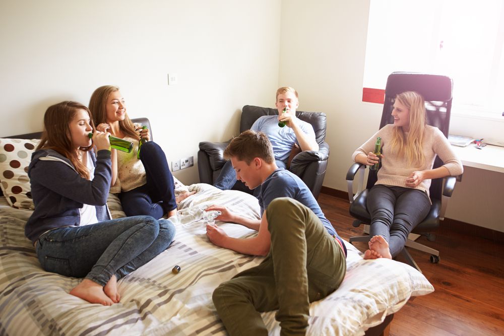 Teenagers sit around in someone&#039;s bedroom, drinking alcohol.