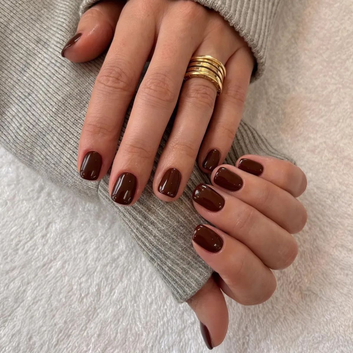 A woman wearing a grey jumper with a short, maroon manicure