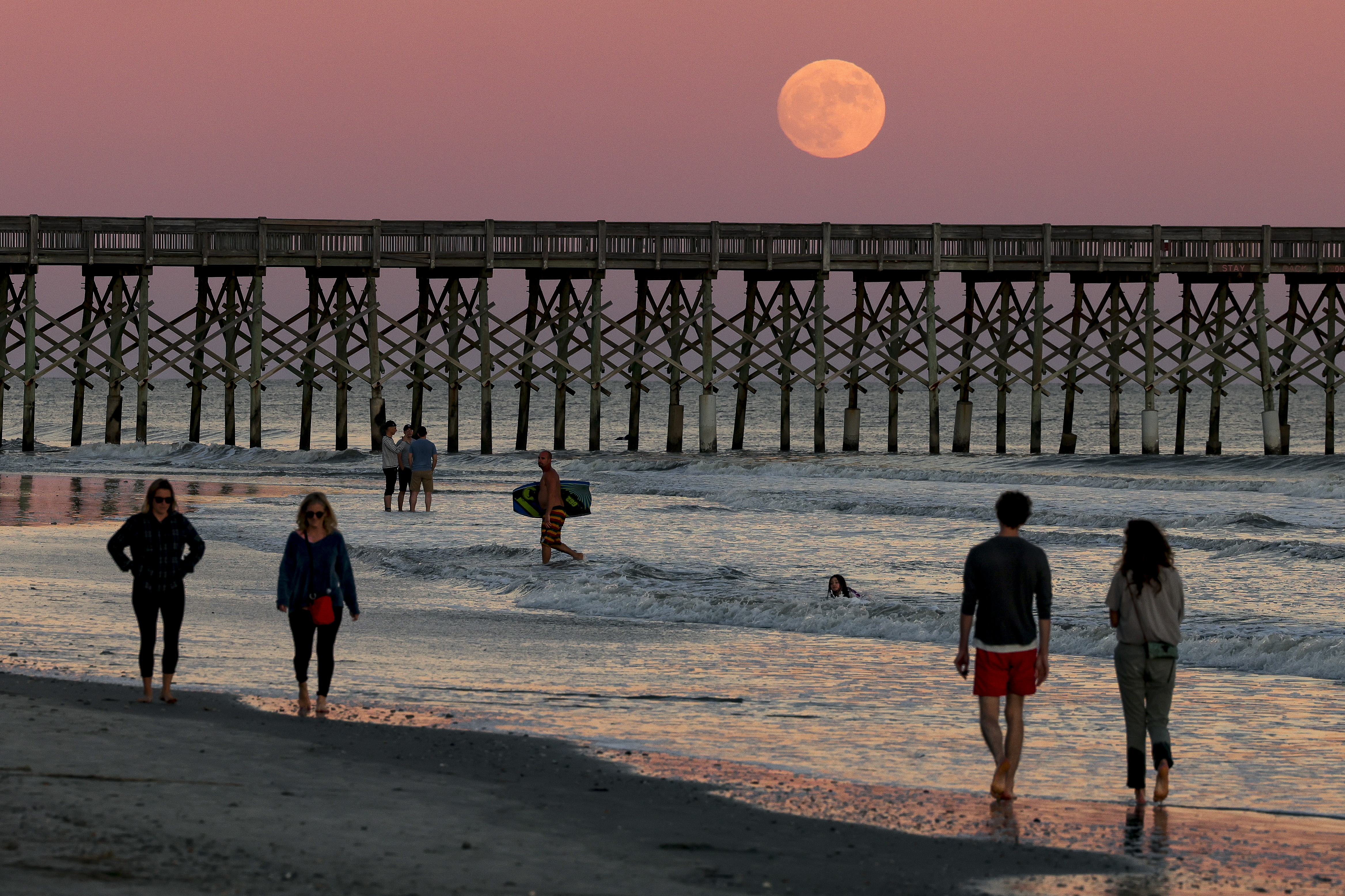 People walk along Folly Beach at sunset