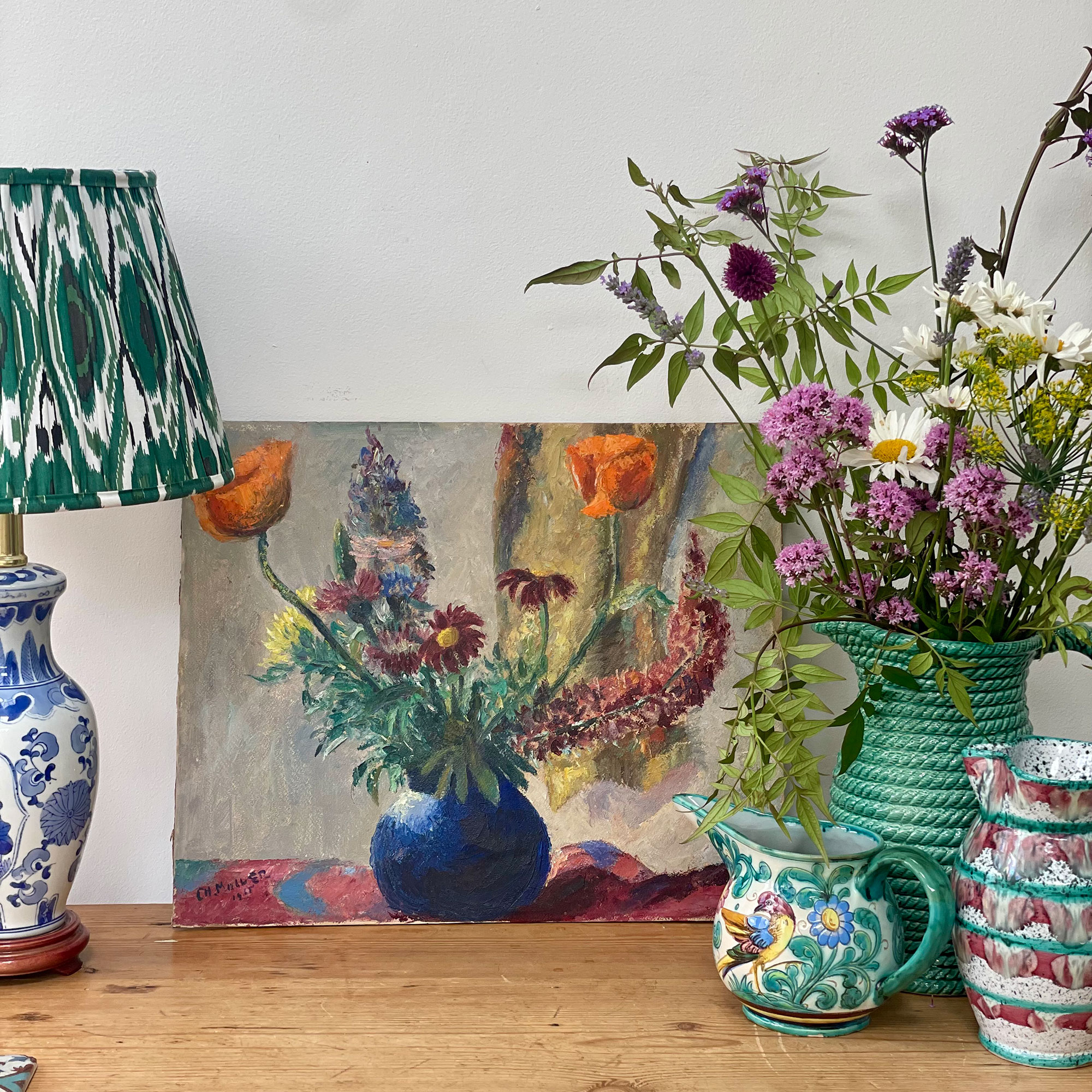 Painting of vase of flowers beside lamp and three painted jugs, one full of fresh flowers