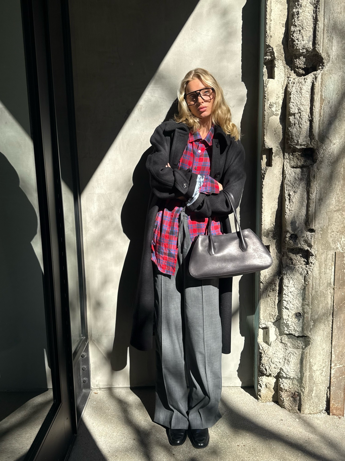 Elsa Hosk wears a flannel shirt, black coat, grey trousers and carries The Row Alger tote bag