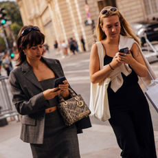 two women wearing sunglasses on their heads looking at their phones while walking on the street 