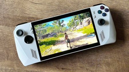 Asus ROG Ally on woodgrain table with Assassin's Creed Odyssey gameplay on screen