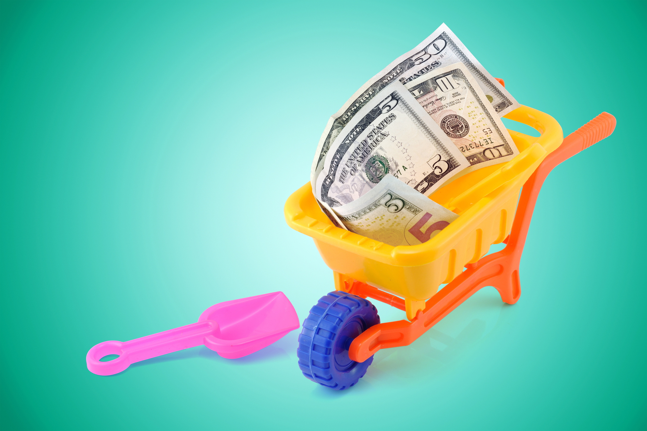 toy wheelbarrow and shovel with U.S. bills inside on a green background