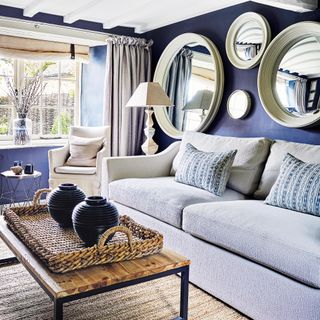 living room with deep blue wall, light grey sofa and a gallery wall of round mirrors