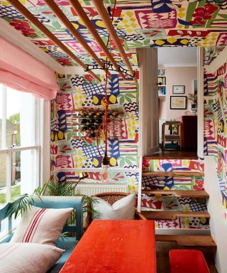 dining room with colorful patterned wallpaper, blue bench and orange table