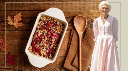 A cut out of Mary Berry in a pink dress in front of a crumble in a tray on a wooden background with a spoon and autumn leaves