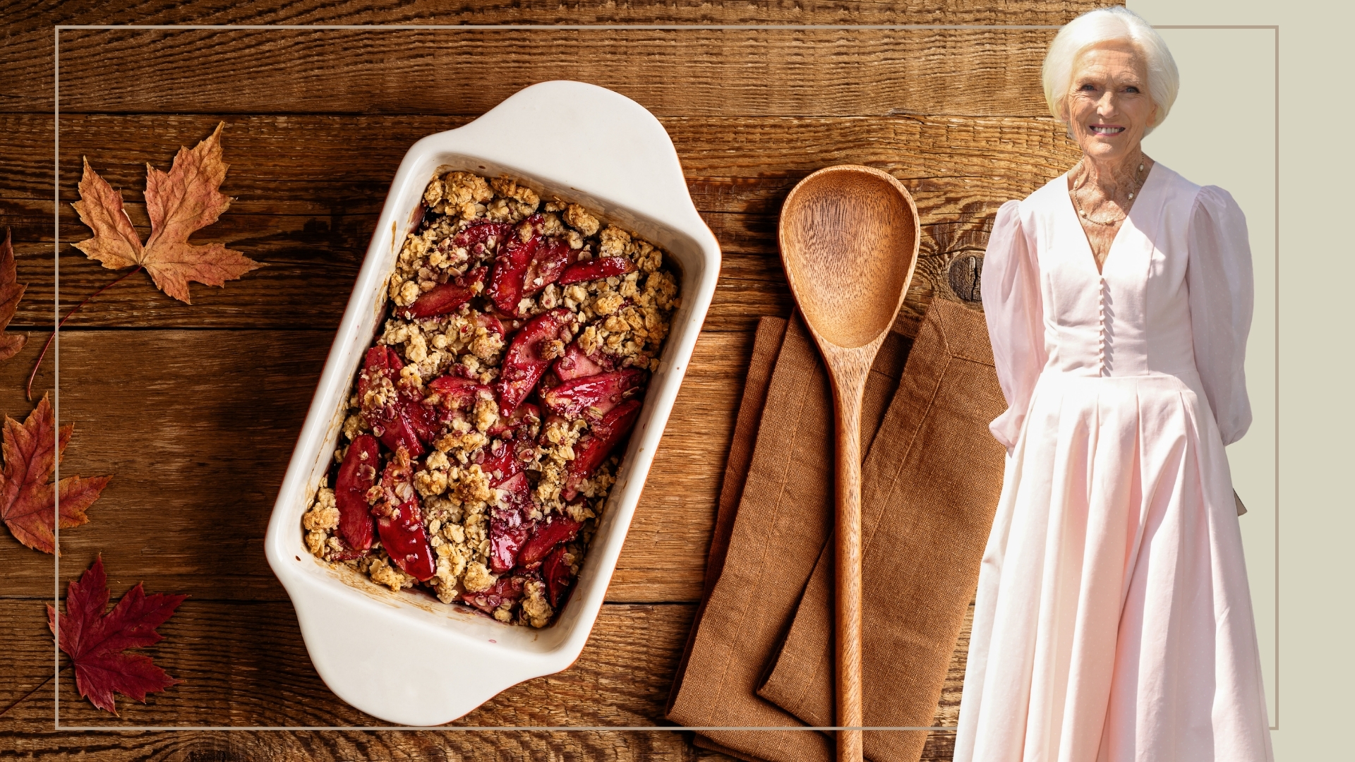 A cut out of Mary Berry in a pink dress in front of a crumble in a tray on a wooden background with a spoon and autumn leaves