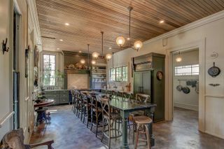 A gothic style kitchen with a long banquette table bar with wooden seating and green cabinetry