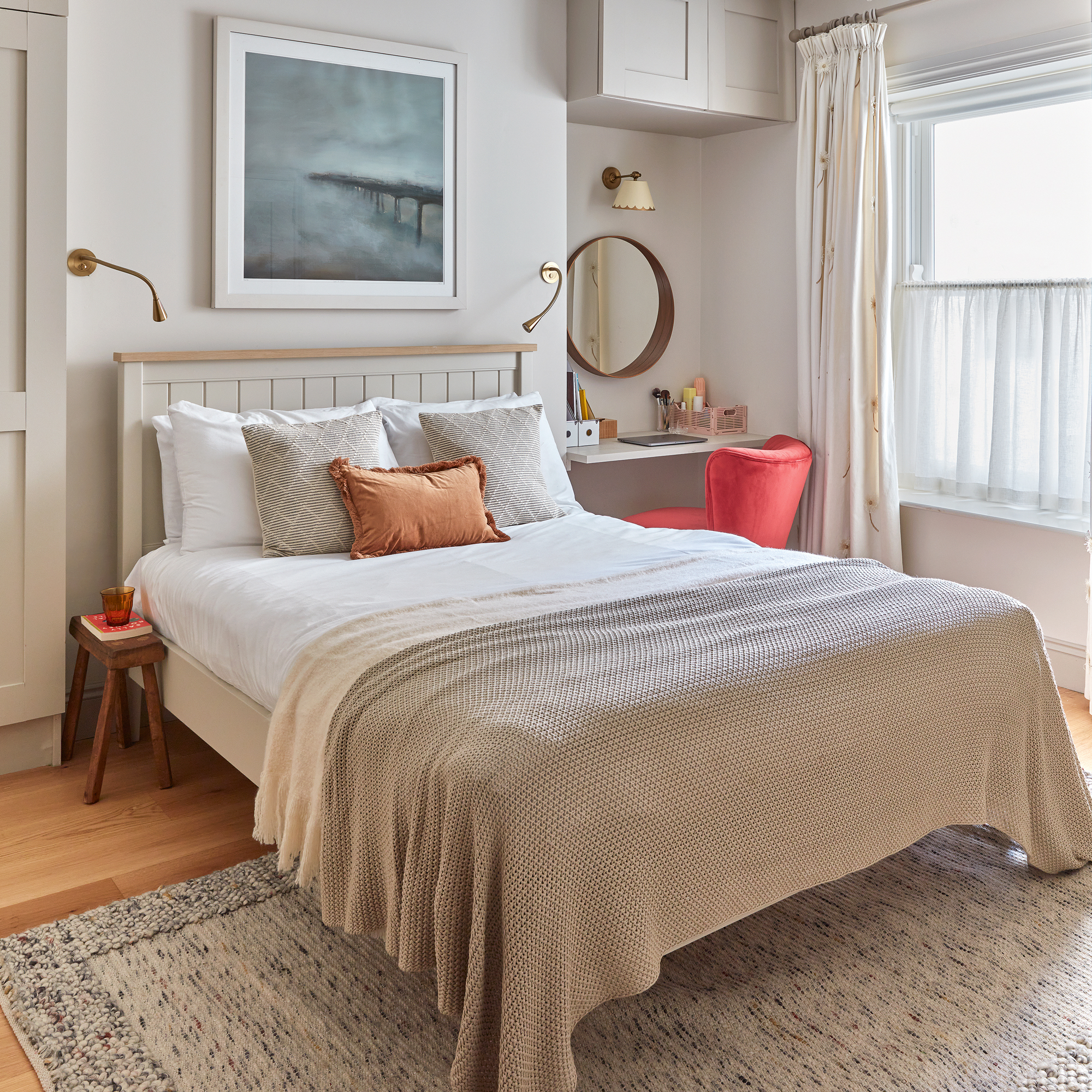 a neutral coloured small bedroom with double bed, an alcove dressing table with a bold red chair