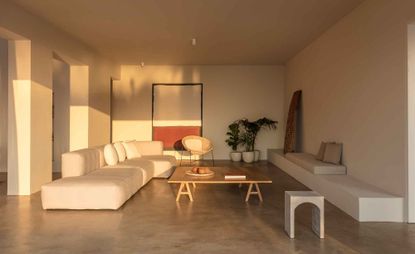 A sitting area with long white sofas, a wooden coffee table and potted plants.